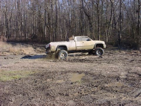 1989 Ford Bronco - A lifted pickup truck navigates a muddy, wooded area, sending mud flying.