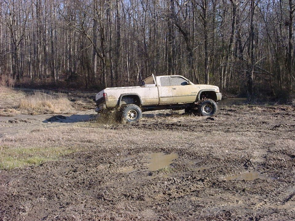 Lifted pickup truck kicking up mud on a wooded trail