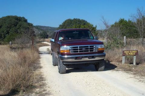 1996 Ford Bronco - This maroon 1996 Ford Bronco, equipped with a body lift, navigates a dirt road leading to a 'Road Closed to Public' sign.
