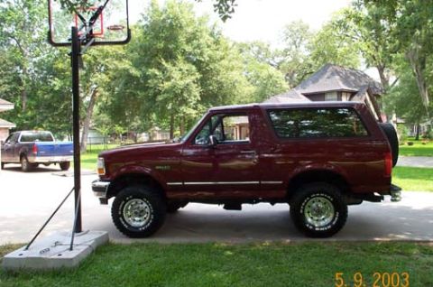 1996 Ford Bronco - Full side profile of a dark red two-door Ford Bronco with a removable hardtop, lifted suspension, chrome five-spoke wheels and all-terrain…