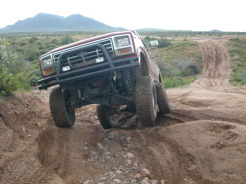 1984 Ford Bronco - A Ford Bronco navigates a challenging off-road trail with steep inclines and loose dirt.