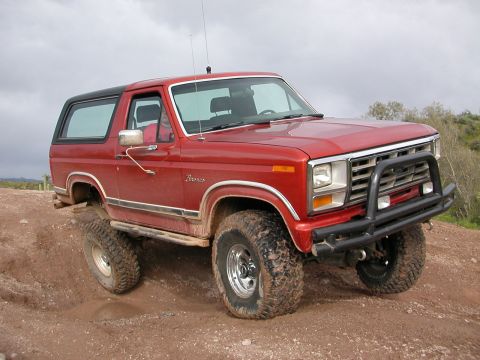 1984 Ford Bronco - A red Ford Bronco with off-road tires navigates a dirt path.