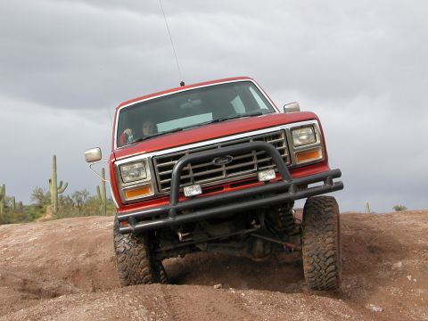 1984 Ford Bronco - Red Ford Bronco navigating an off-road trail with cacti visible.
