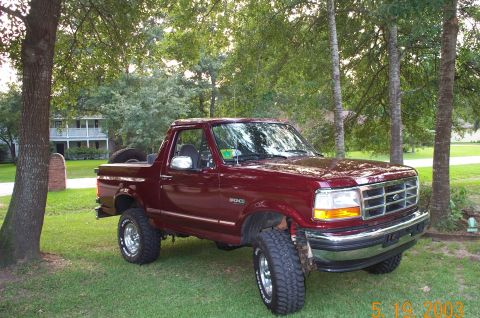 1996 Ford Bronco - Dark red Ford Bronco with the rear hardtop removed, showing the open bed area and a spare tire behind the cab, sitting on a grassy lawn wit…