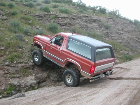 1984 Ford Bronco - This red Ford Bronco is navigating a steep dirt path, its off-road capabilities.