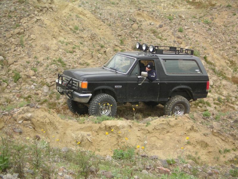 Black Ford Bronco climbing a dirt hill, driver visible inside