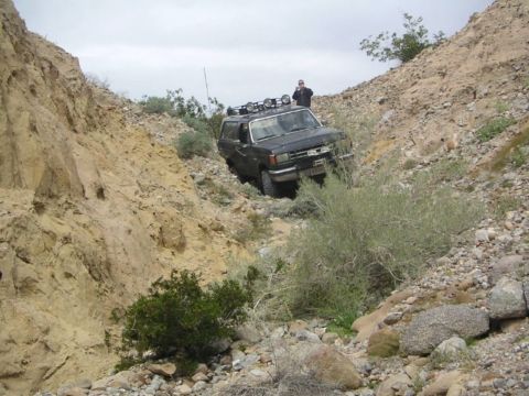 1988 Ford Bronco - Ford Bronco tackling a challenging off-road path in a desert canyon environment.