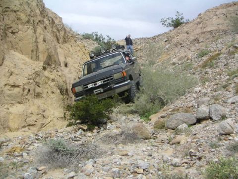 1988 Ford Bronco - A modified Ford F-150 navigates a steep, rocky trail with a person observing from above.