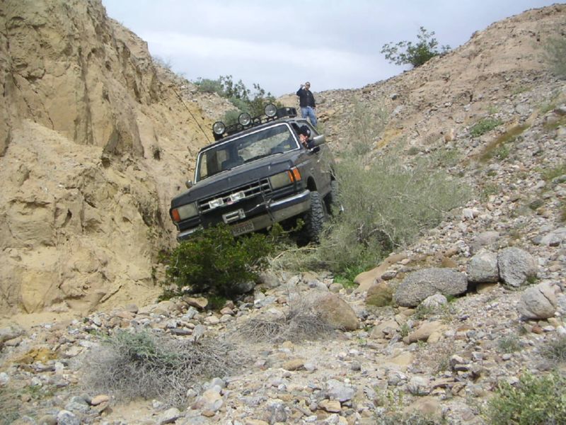 Black 1987 Ford F-150 driving up a rocky hill, with a person standing on the ridge above