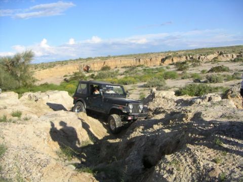 1988 Ford Bronco - A black Jeep Wrangler TJ is shown off-roading through a , rocky landscape under a blue sky.