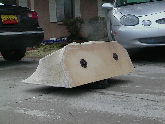 Fiberglass body kit part on concrete, with a silver car and a black car in the background