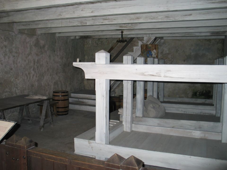 Interior of a room with wooden beams, a table, a barrel, and a large white wooden structure