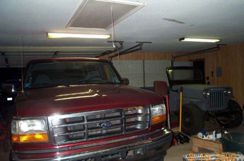 1996 Ford Bronco - A dark red 1990s Ford truck sits nose-out in a home garage with its chrome grille and amber turn lamps under fluorescent lighting, sharing…