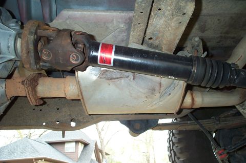1996 Ford Bronco - Underside view of a lifted 4x4 showing a new black double-cardan (CV) driveshaft with a red decal and rubber slip-yoke boot running past a…