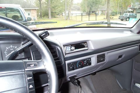 1996 Ford Bronco - Gray interior dashboard of a Ford truck showing steering wheel, aftermarket radio, climate controls and view out the windshield.