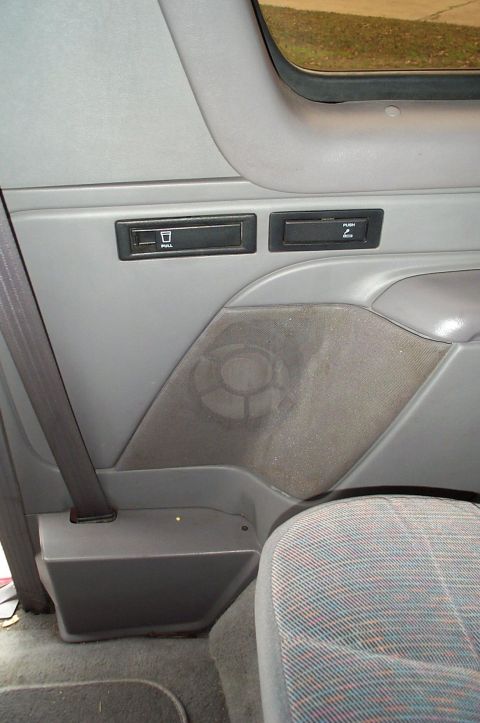 1996 Ford Bronco - Gray interior rear side panel of an SUV showing a rear speaker grille, a pull-out cupholder marked PULL and a PUSH ashtray door, with the s…