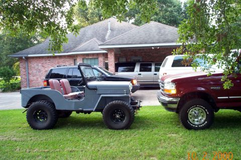 1954 Jeep Wrangler - A gray Jeep is parked in front of a house with other vehicles.