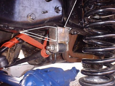 1988 Ford Bronco - Under-front-end close-up of a fabricated bare-steel shock or limit-strap mount welded to the frame, with a bolt through a bushed eye and an…