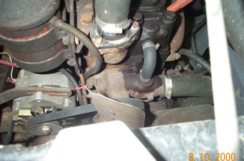 1954 Jeep Wrangler - Close-up of engine components including alternator, hoses, and fan belt. Fluid leak apparent.