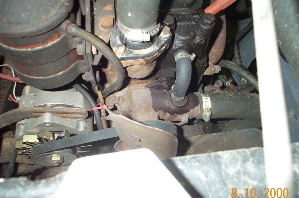 Engine bay detail showing alternator, belts, hoses, and engine block. Some fluid leakage is visible