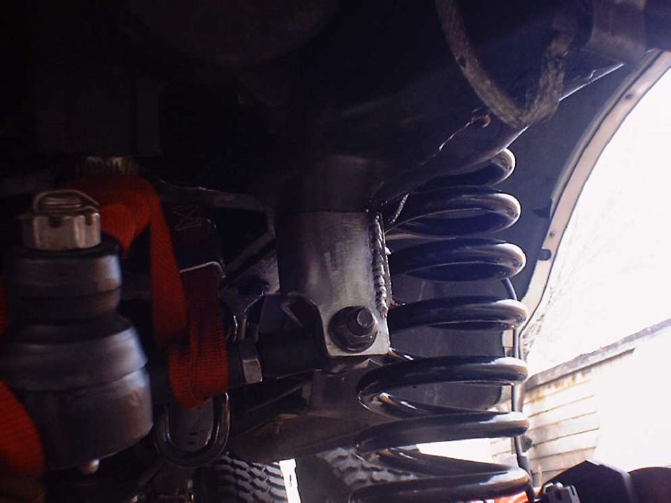Close-up of a vehicle's coil spring and suspension linkage, with a red strap visible