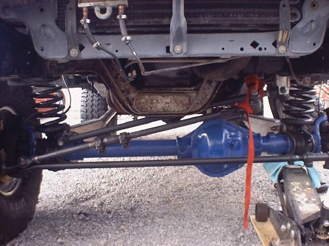 1988 Ford Bronco - Underside view of a vehicle's front axle and suspension system, showing the differential and steering linkage.