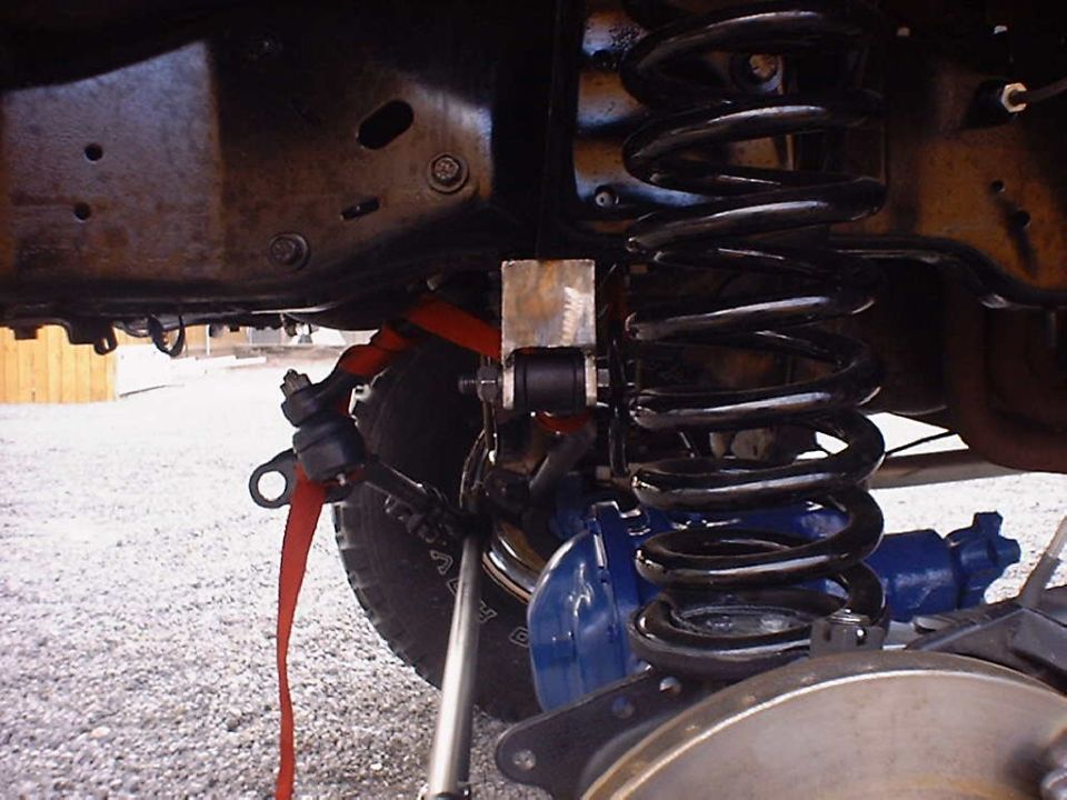 Close-up of a vehicle's front suspension with a large coil spring, red strap, and blue brake caliper visible