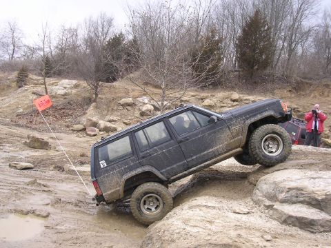 1995 Jeep Cherokee - A black Jeep Cherokee navigates a rocky, muddy off-road course with another vehicle visible in the background.