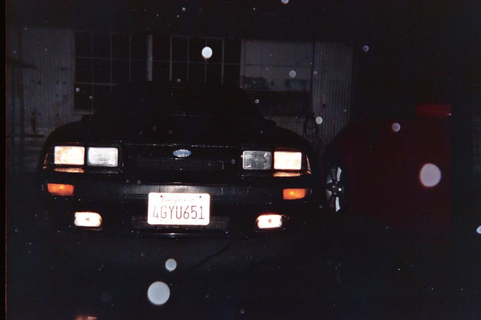 Black Fox-body Mustang front end at night with quad headlights and fog lamps lit