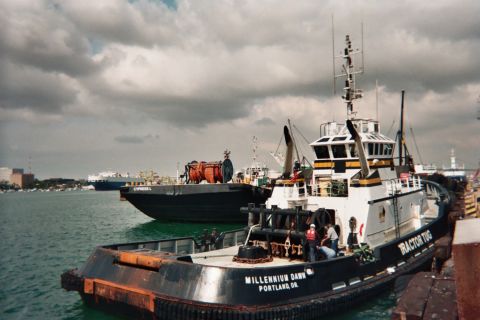 1990 Ford Bronco - Two tugboats sit in a harbor under cloudy skies, the foreground one lettered 'Millennium Dawn, Portland, OR'.