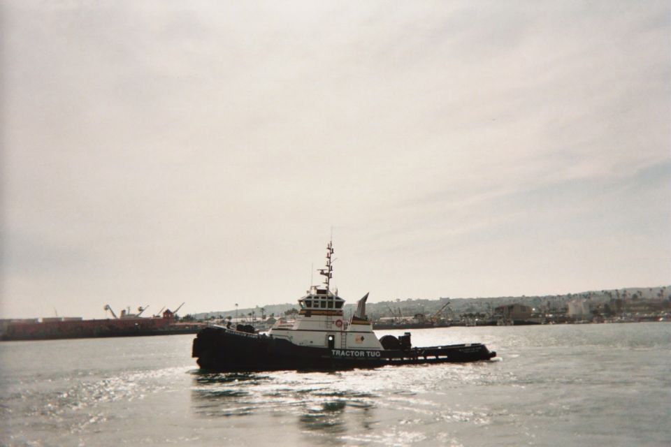 Black-hulled tractor tug under way in a harbor near a port