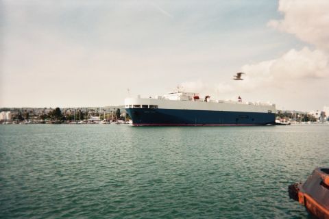 1990 Ford Bronco - large blue roll-on car-carrier ship glides through a harbor under a partly cloudy sky as a gull flies past.