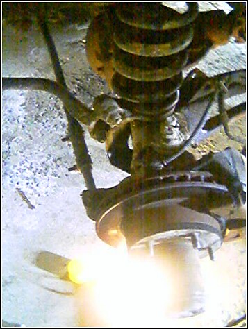 1993 Ford Bronco - Low-angle close-up of a truck's front suspension with the wheel off, showing the coil spring, radius arm and shock absorber above the expos…