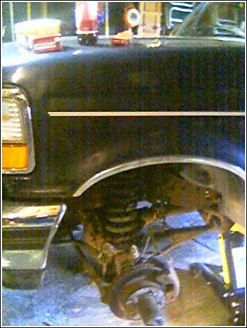 1993 Ford Bronco - Dark full-size Ford truck up on a jack in a garage with the front wheel removed, exposing the coil spring, radius arm and hub of the front…