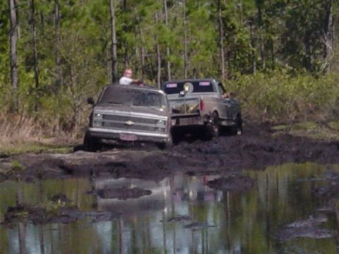 1989 Ford Bronco - Two trucks are stuck in the mud, with one driver visible above the dashboard.