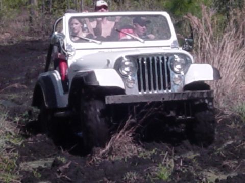 1989 Ford Bronco - White Jeep CJ-7 navigates a muddy off-road trail with occupants.