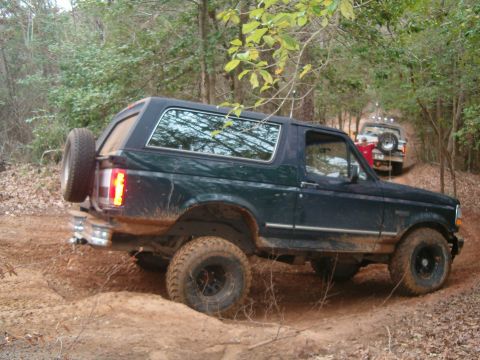 1996 Ford Bronco - A dark green Ford Bronco navigates a muddy trail with another vehicle following closely behind.
