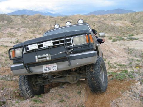 1988 Ford Bronco - This black SUV, likely from the 1980s, navigates a challenging off-road terrain with its winch and light bar engaged.