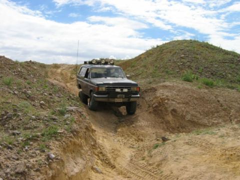 1988 Ford Bronco - SUV navigates a steep dirt path with a large hill to the right and a cut-away to the left.