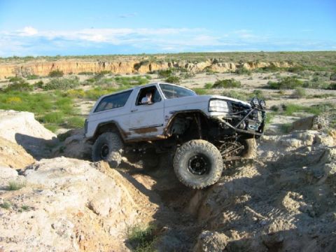 1988 Ford Bronco - Modified SUV tackles challenging off-road obstacles under a clear blue sky.