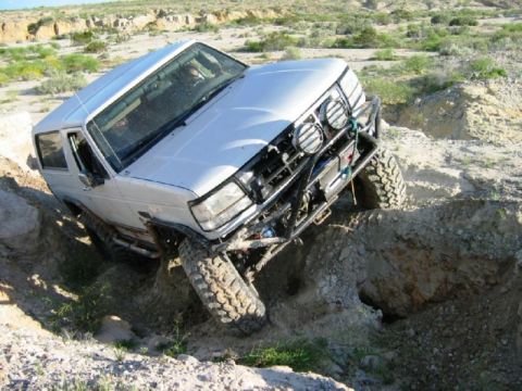 1988 Ford Bronco - Silver SUV navigating a challenging off-road terrain with one wheel in a deep ditch.