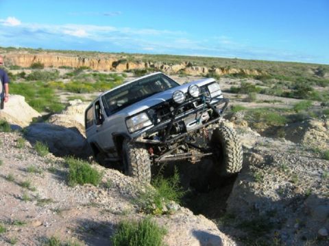 1988 Ford Bronco - This heavily modified SUV tackles a challenging off-road obstacle with its front wheels high in the air.