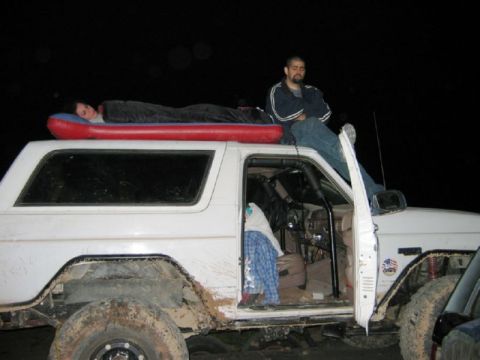 1988 Ford Bronco - A white Ford Bronco with two people on its roof is parked at night.