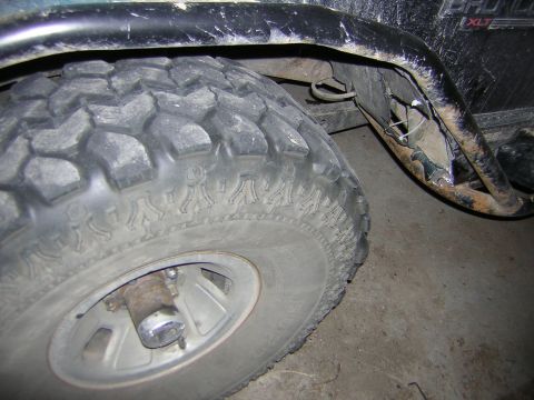 1995 Ford Bronco - Close-up of a 1995 Ford Bronco's rear tire and a damaged fender flare showing rust and exposed metal.