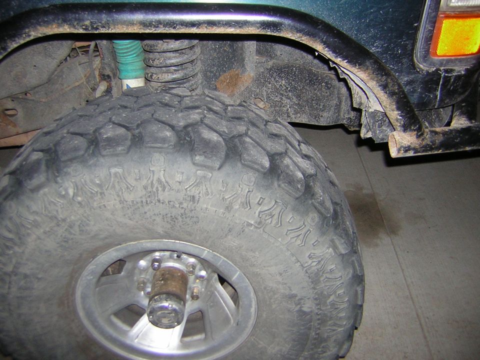 Green SUV wheel well with large off-road tire, black fender flare, and part of a bumper