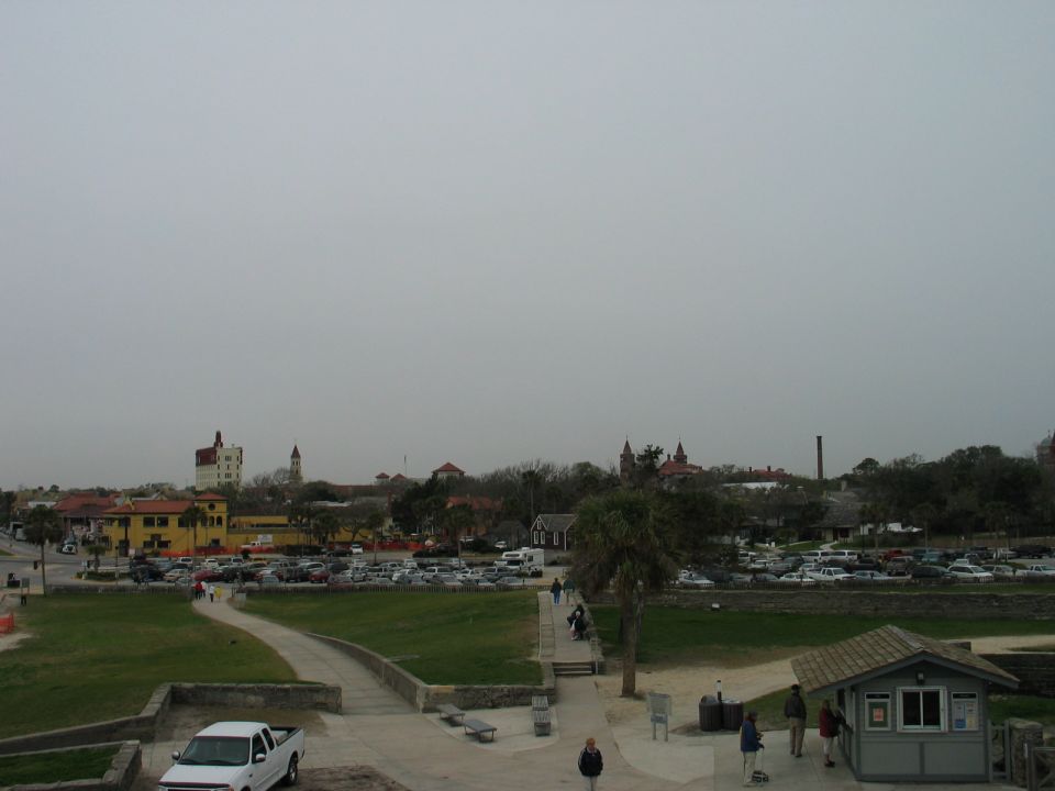 White pickup truck parked near a path with a large parking lot and buildings in the background