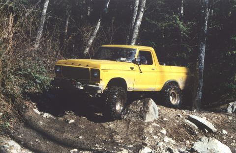 1990 Ford Bronco - This yellow pickup truck is navigating a challenging off-road path through a forest.