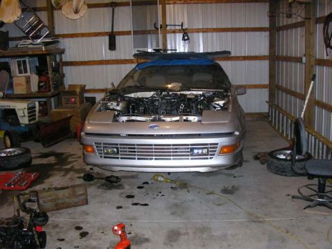 1990 Ford Probe - A silver 1990 Ford Probe sits in a garage with its hood open, undergoing maintenance.