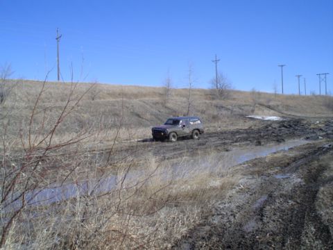1981 Ford Bronco - 1981 Ford Bronco tackling a challenging muddy terrain under a bright blue sky.