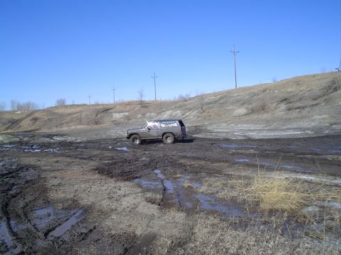 1981 Ford Bronco - A Ford Bronco navigates a challenging muddy terrain under a clear blue sky.